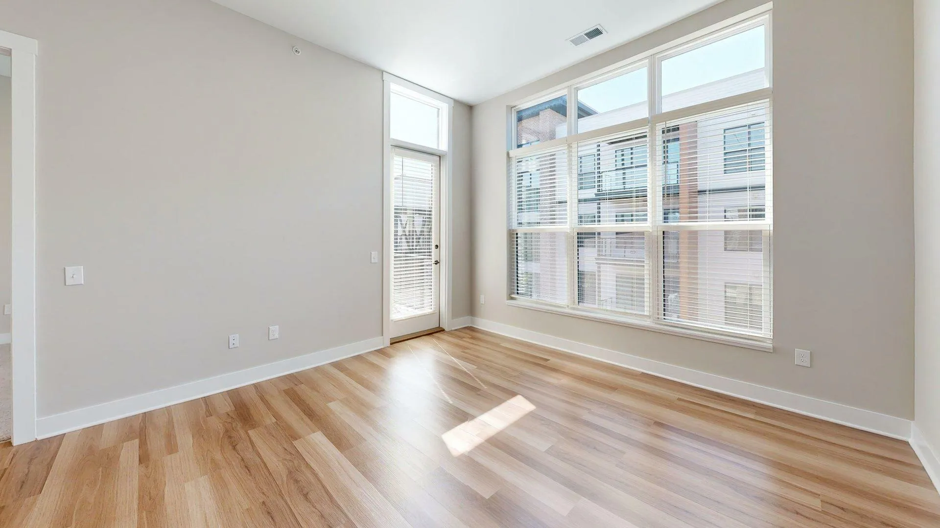 Bright apartment room with large windows, wood flooring, and a private door to a balcony, perfect for natural light lovers.
