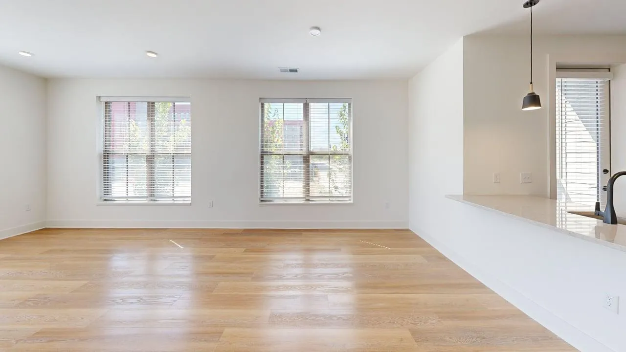 Bright and airy living space with large windows and sleek hardwood floors, adjacent to a modern kitchen with a stylish pendant light.