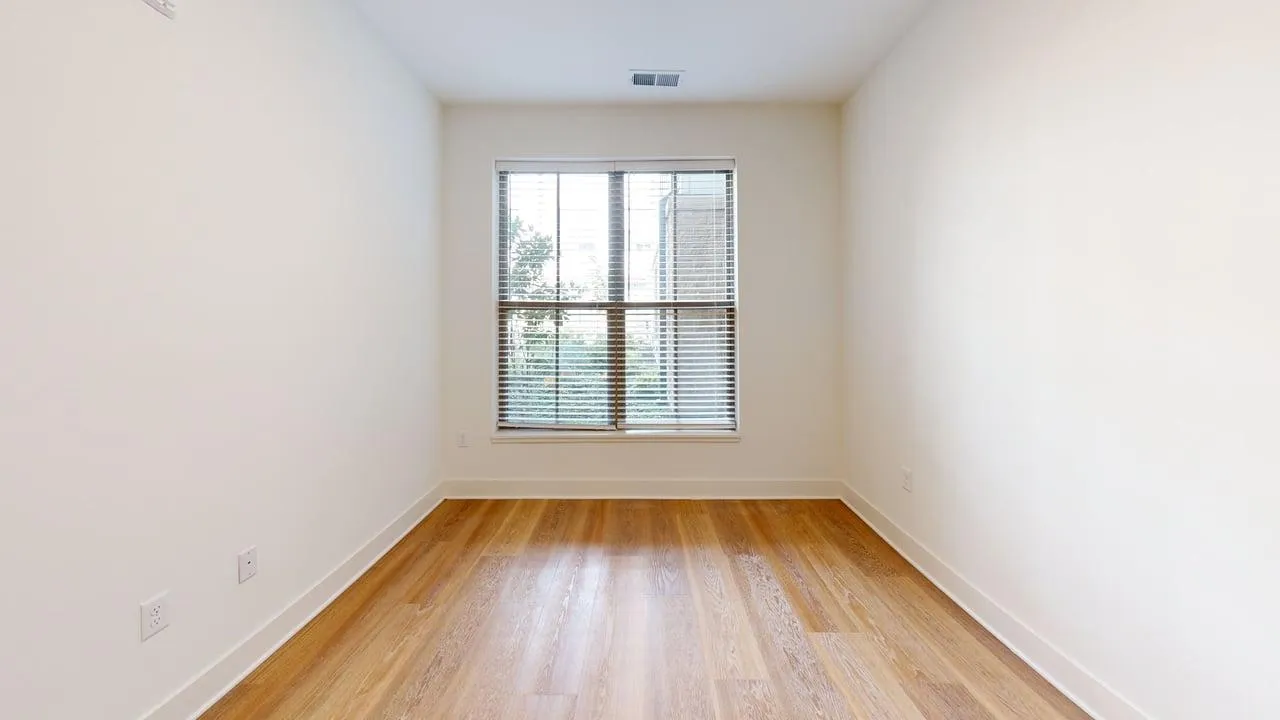 Bright room featuring a large window with blinds, showcasing sleek hardwood floors and clean white walls.