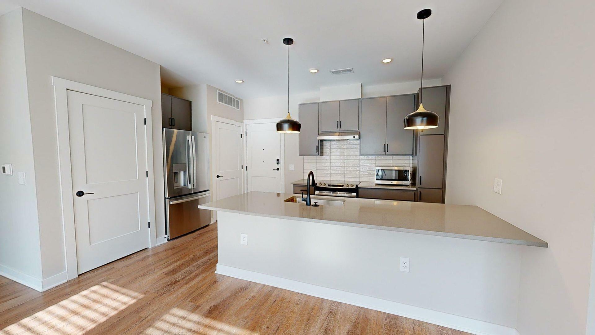 Modern kitchen with sleek gray cabinets, stainless steel appliances, and elegant pendant lighting over a spacious bar counter.