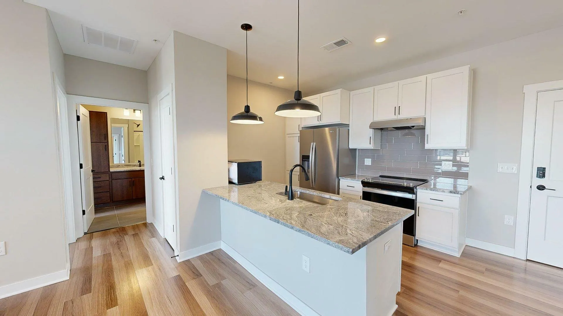 Modern kitchen with sleek countertops, stylish pendant lighting, stainless steel appliances, and elegant wood flooring