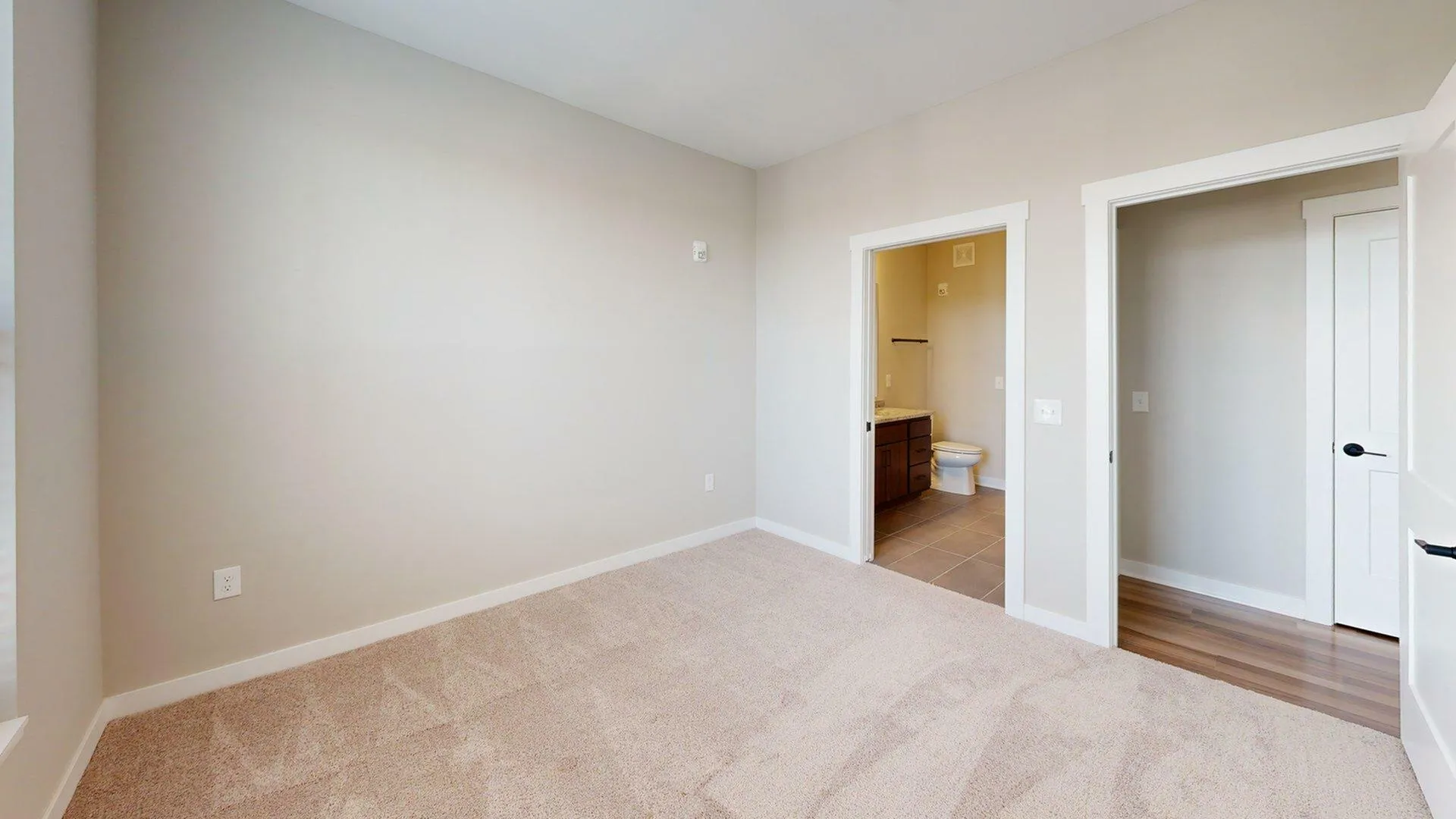 Inviting bedroom with soft carpeting, neutral walls, and a view into a modern, tiled bathroom with elegant fixtures.