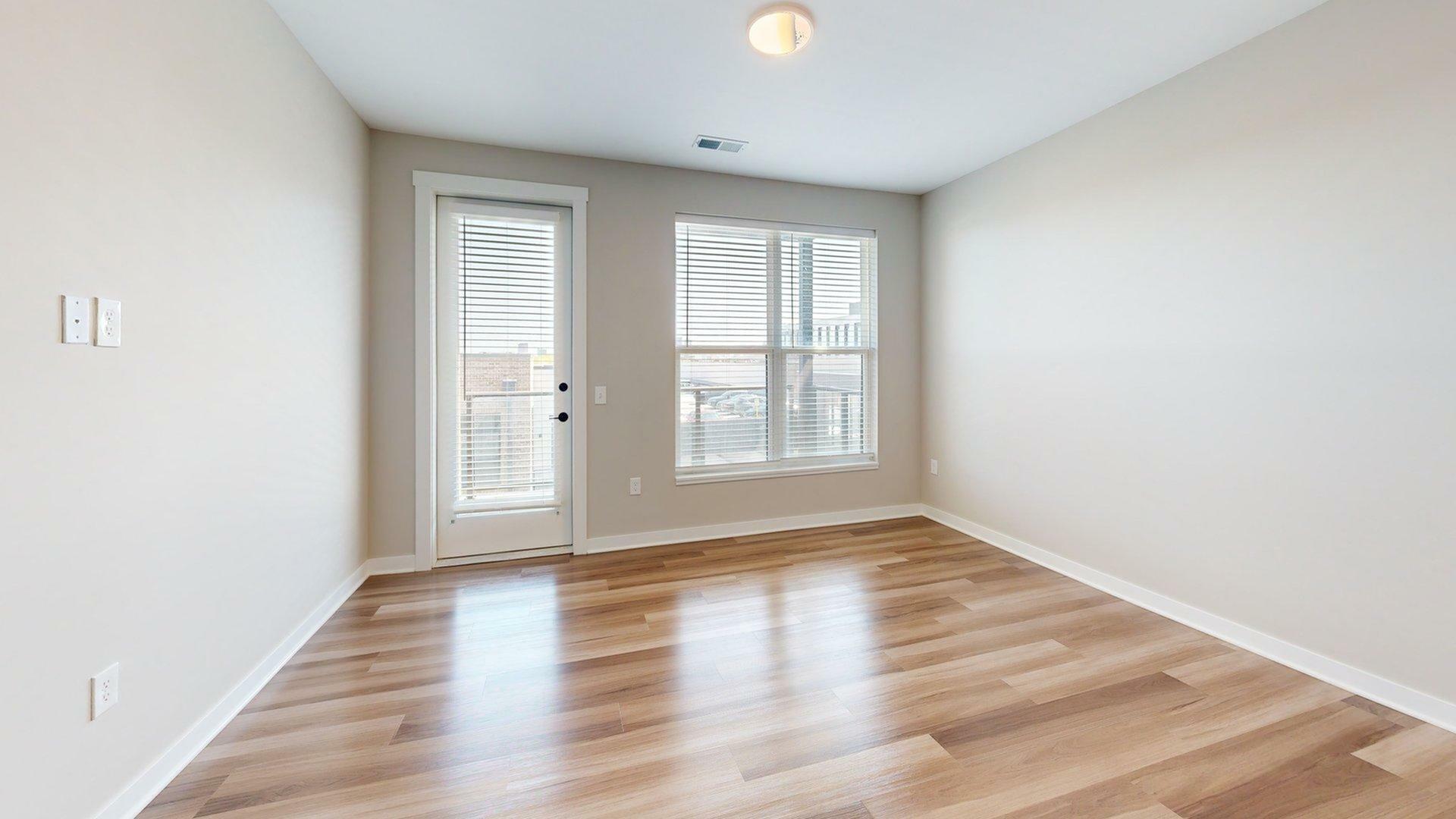 Bright empty room with elegant wood flooring, large windows, and a door leading to a balcony, perfect for customization and creative design.