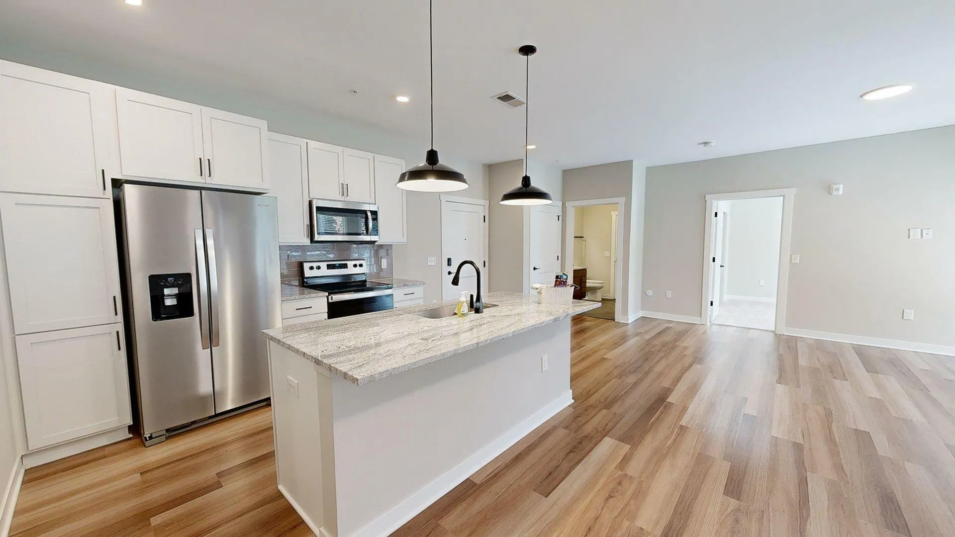 Bright and modern open-concept kitchen and living area with stainless steel appliances, stylish pendant lighting, and sleek hardwood floors.