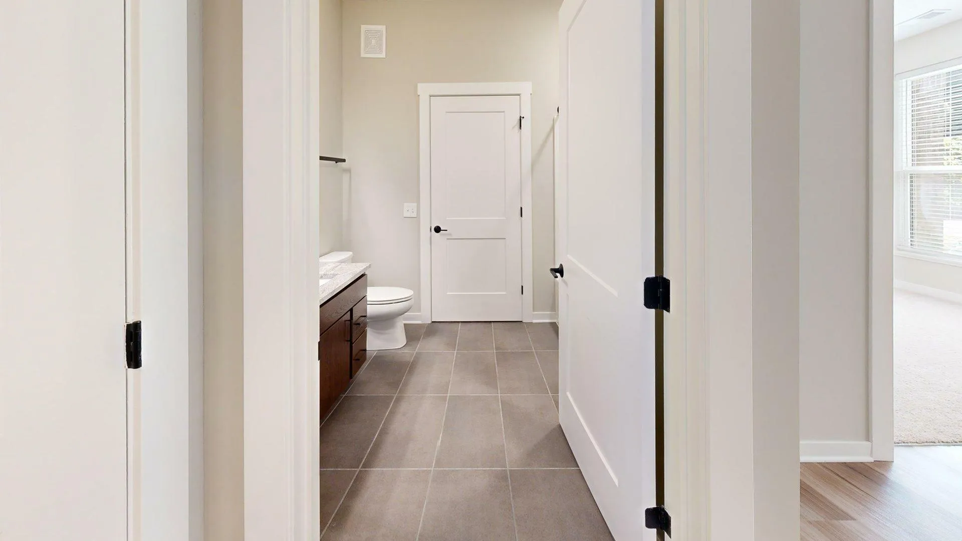 Bright, modern bathroom featuring sleek tile floors, elegant vanity, and a pristine white door leading to a cozy, sunlit room.