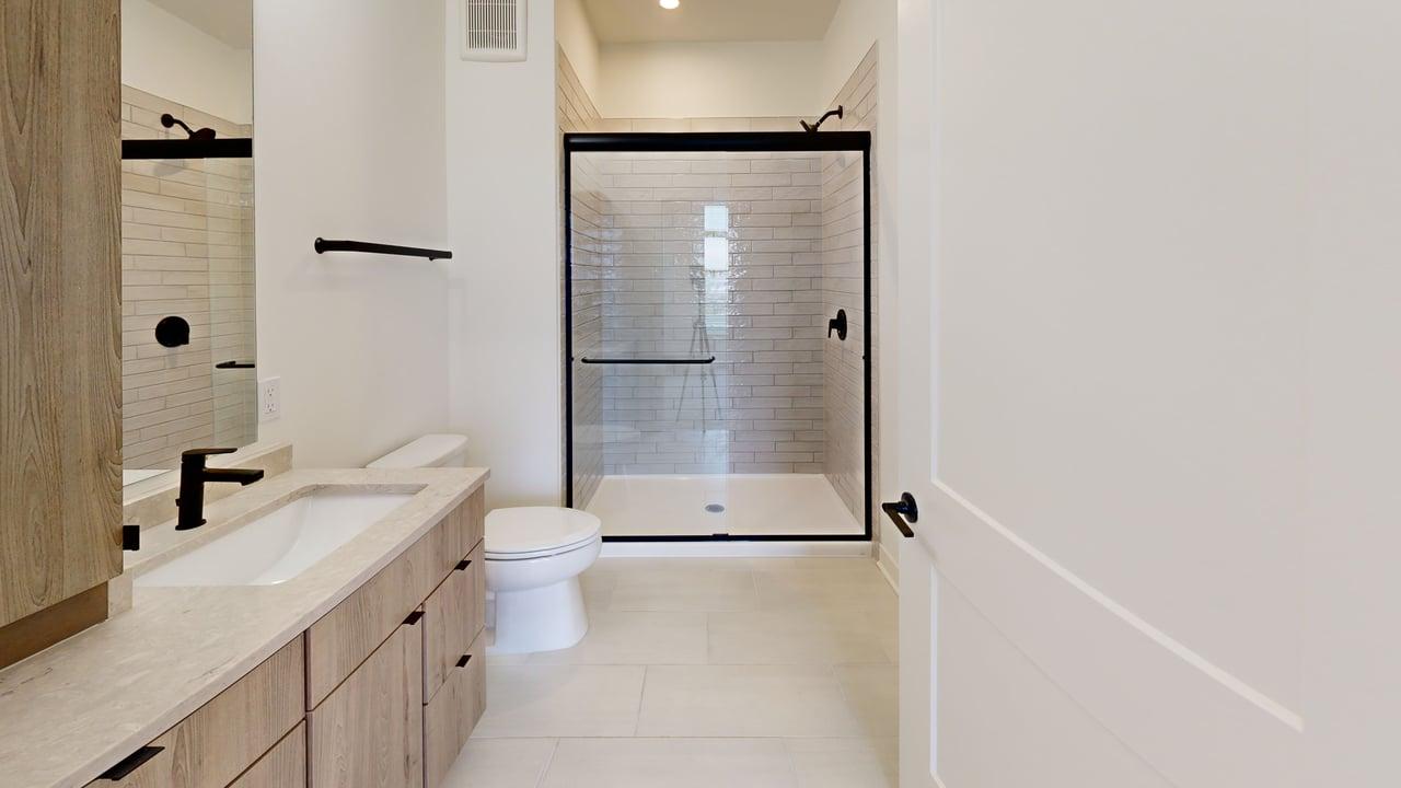 Modern bathroom with a spacious glass-enclosed shower, wooden vanity, and elegant fixtures.