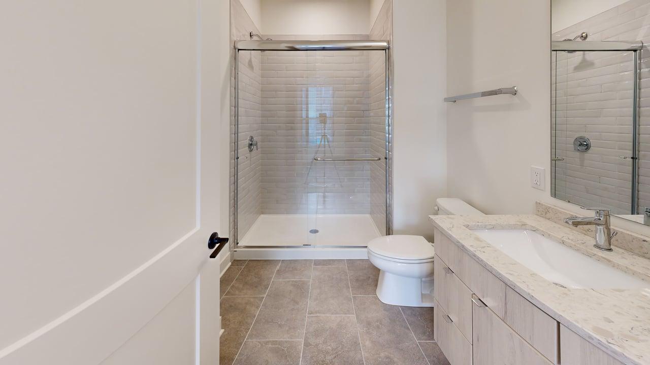 Elegant bathroom featuring a spacious glass-enclosed shower, modern vanity with marble countertop, and sleek tile flooring.