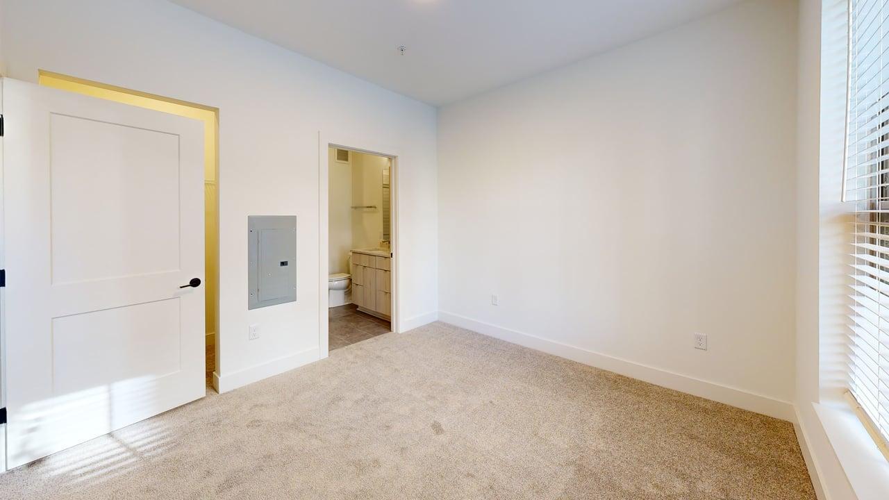 Bright, spacious bedroom with plush carpeting, modern en-suite bathroom, and ample natural light.
