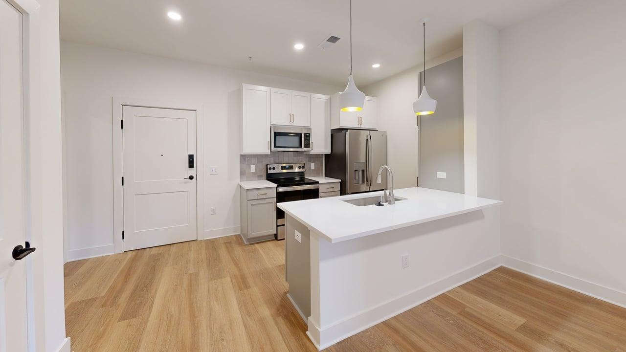 Modern kitchen in an open-concept apartment featuring a sleek island, stainless steel appliances, and bright pendant lighting.