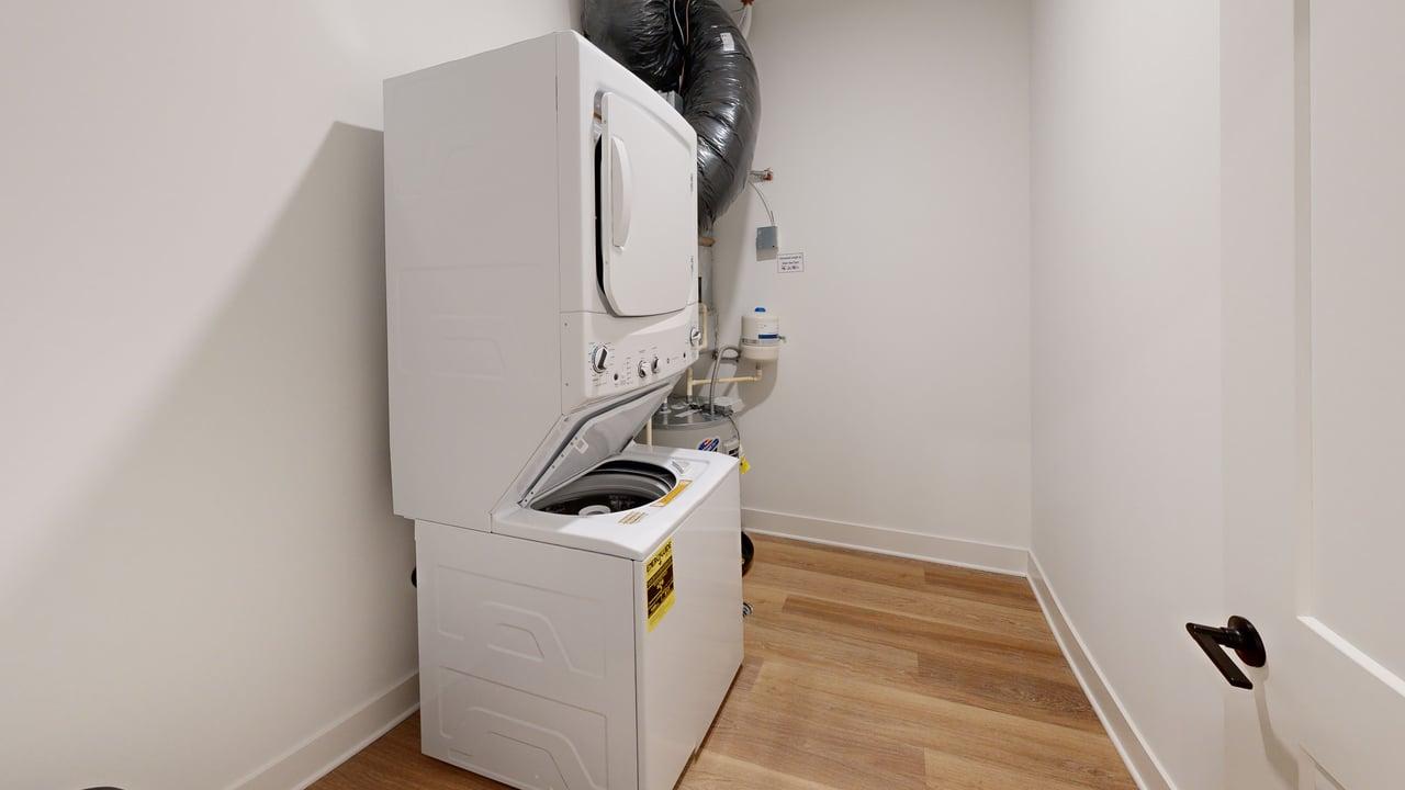 Modern laundry room with stacked washer and dryer, gleaming wooden floor, and tidy layout.