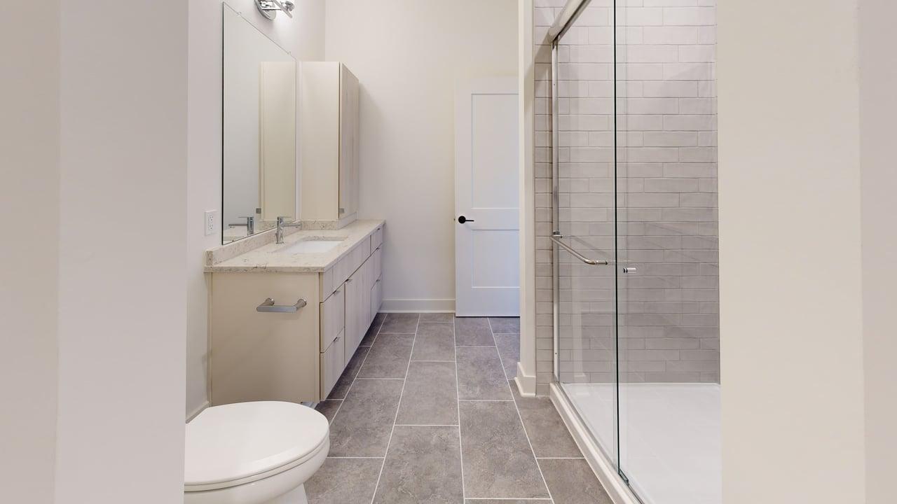 Modern bathroom featuring sleek grey tile flooring, elegant vanity with ample storage, and a spacious glass-enclosed shower.