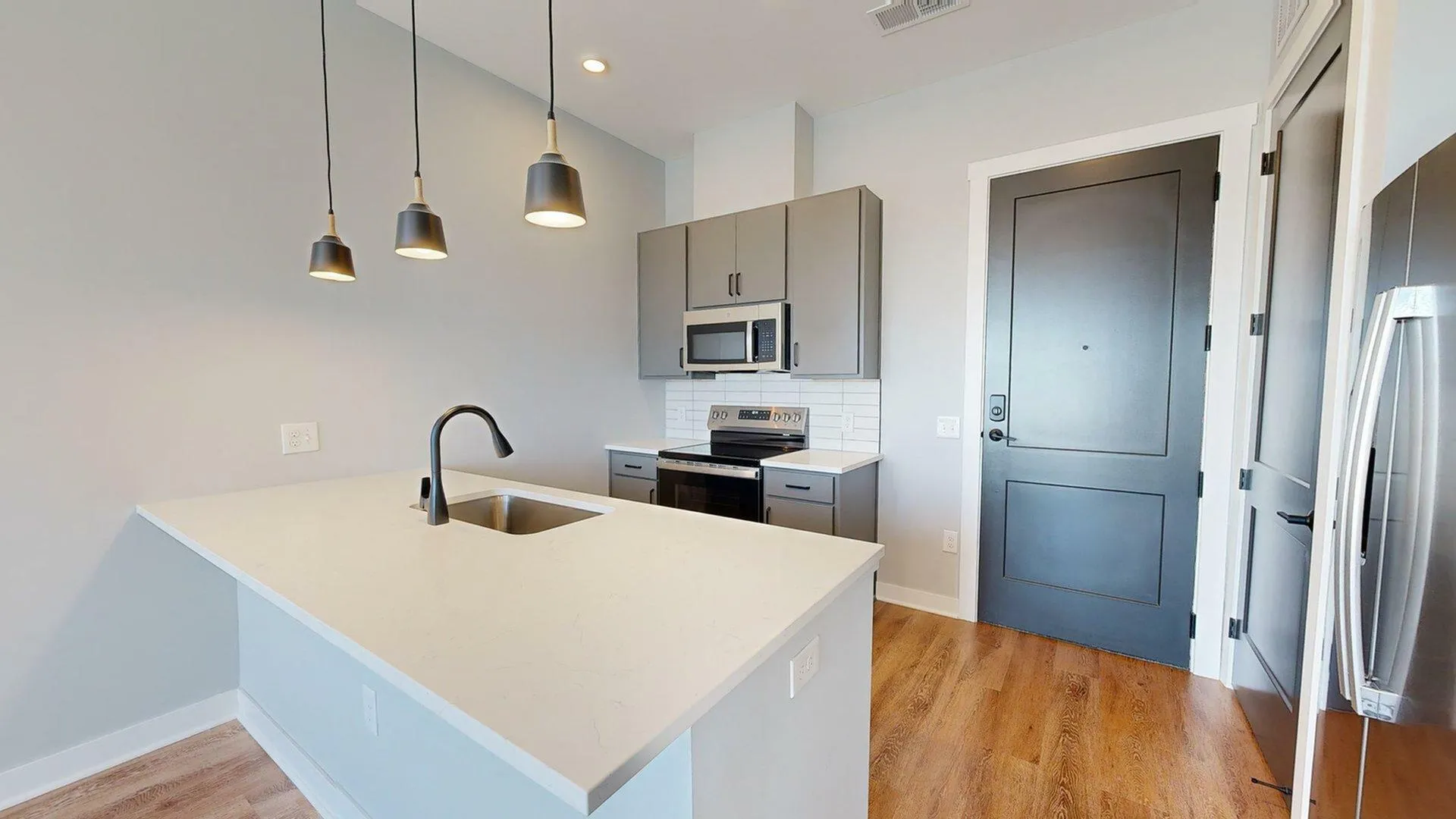 Modern kitchen space with sleek stainless steel appliances, elegant pendant lighting, and a spacious countertop in a contemporary apartment setting.