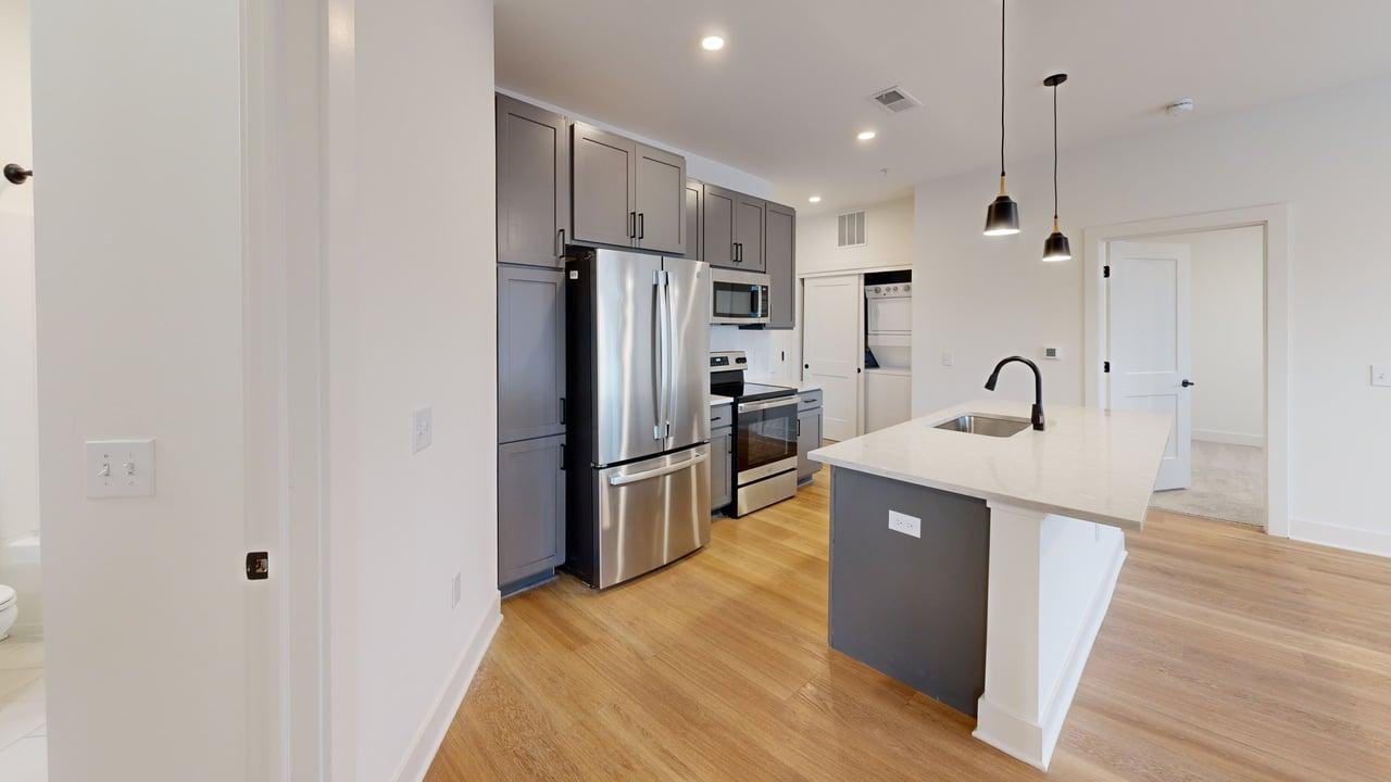 Modern apartment kitchen featuring sleek stainless steel appliances, elegant grey cabinetry, and a stylish island with pendant lighting.