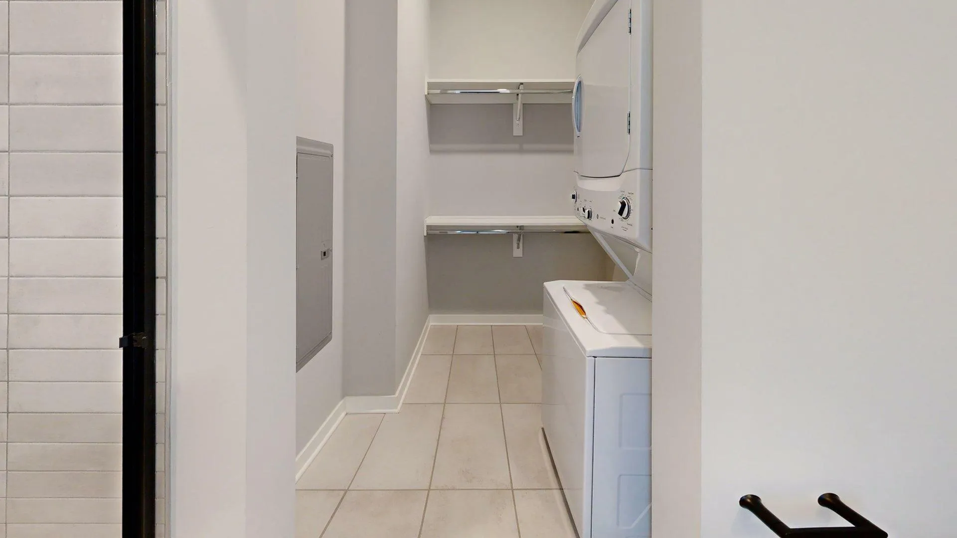 Modern laundry room with stacked washer and dryer, sleek shelving, and contemporary tiled flooring.