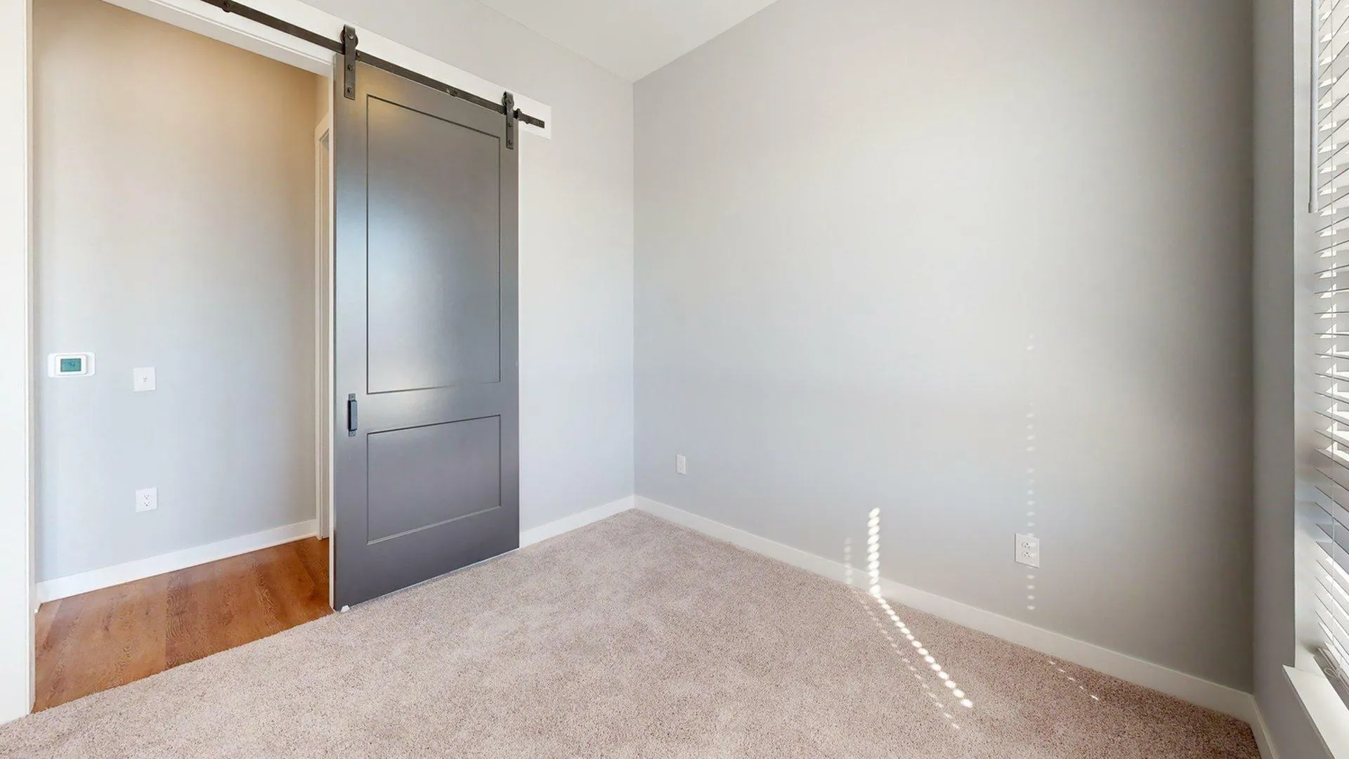Cozy bedroom featuring a stylish sliding barn door and plush carpet, bathed in natural light from an adjacent window.
