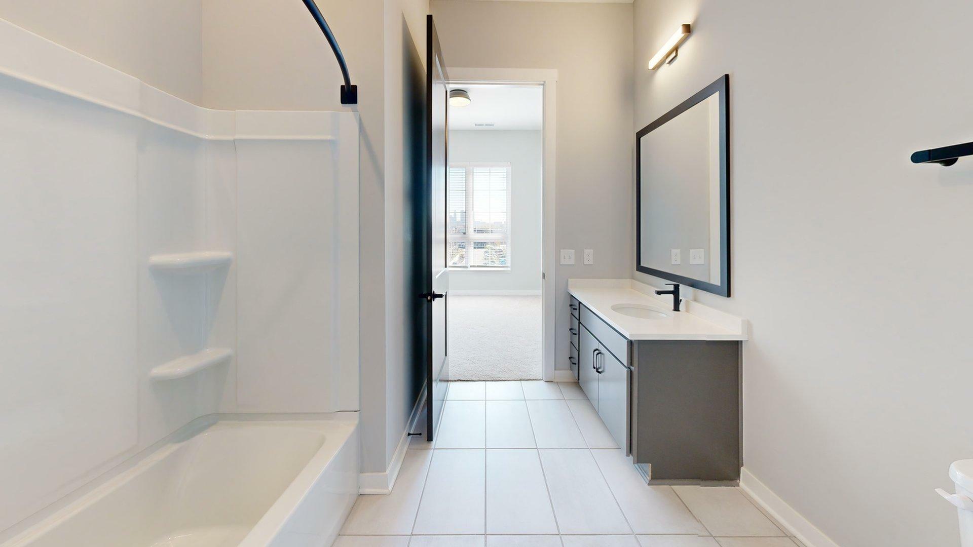 Sleek modern bathroom with large vanity mirror, elegant lighting, and a bright interior leading to a sunlit bedroom.