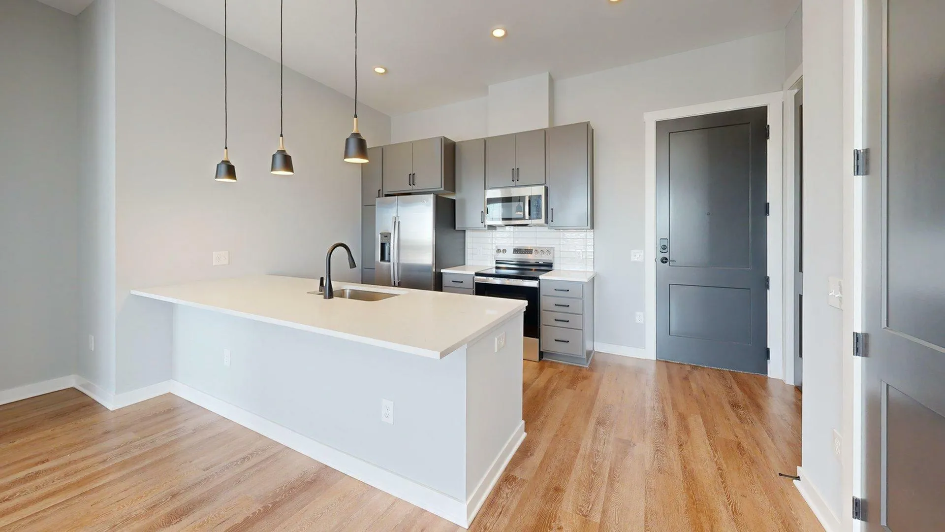 Modern kitchen with sleek gray cabinets, stainless steel appliances, and elegant pendant lighting over a spacious island.