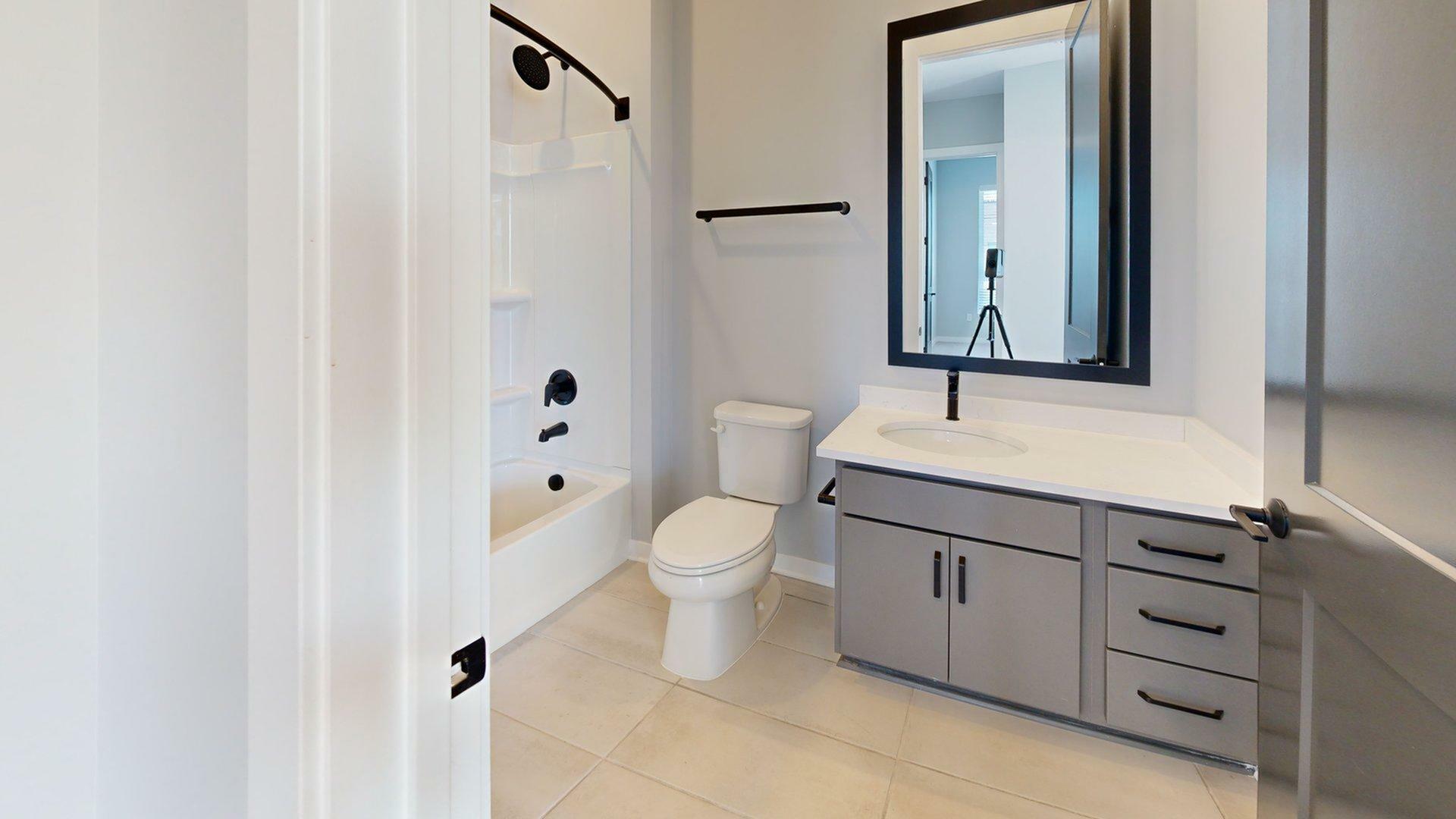 Modern bathroom featuring sleek gray cabinetry, large mirror, and a pristine bathtub. Elegant fixtures add a touch of luxury.