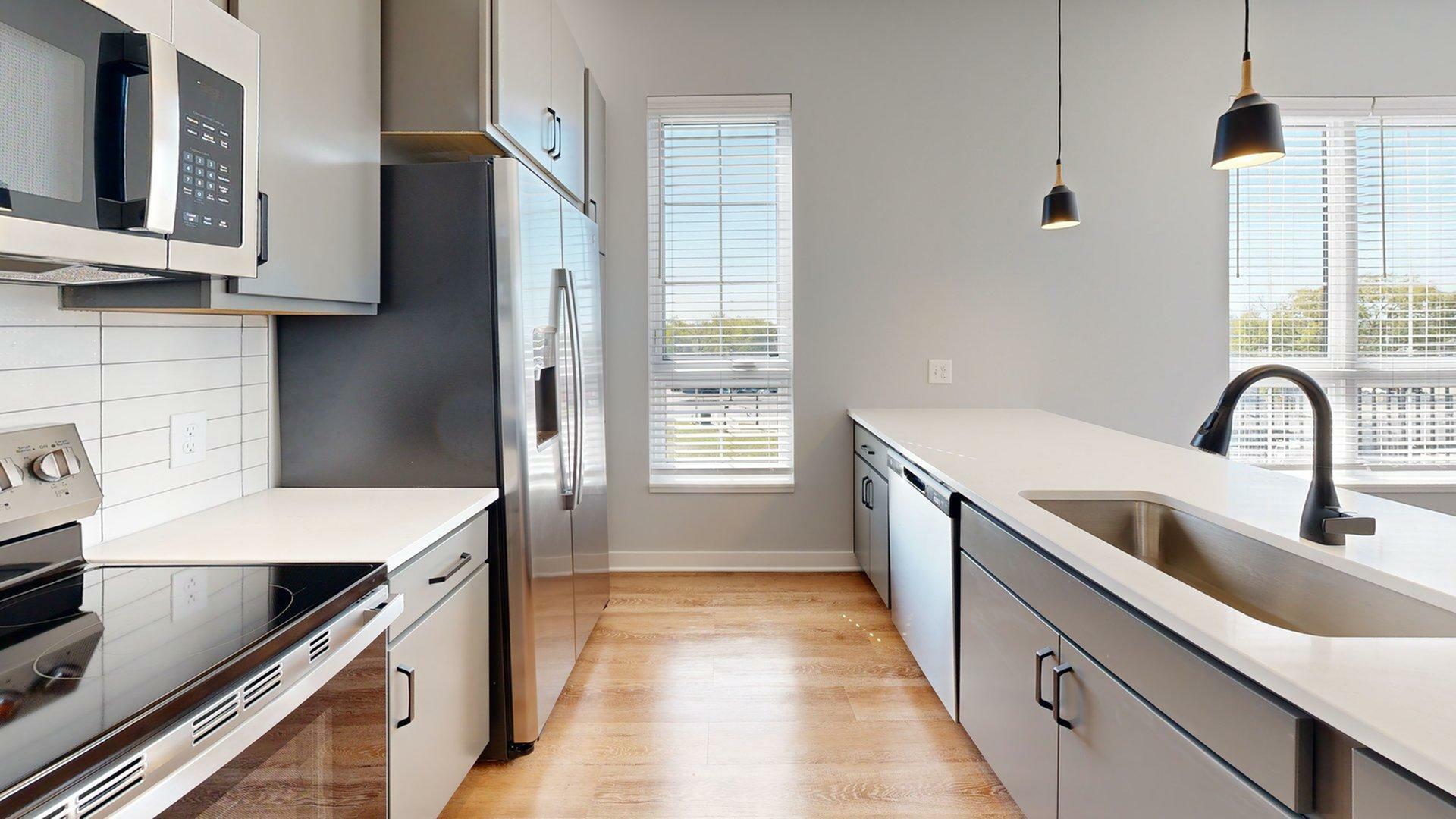 Modern kitchen featuring sleek stainless steel appliances, elegant countertops, and stylish lighting with large windows providing natural light.
