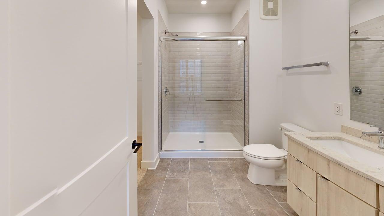 Elegant bathroom featuring modern shower with glass doors, stylish tile flooring, and sleek wooden cabinetry.