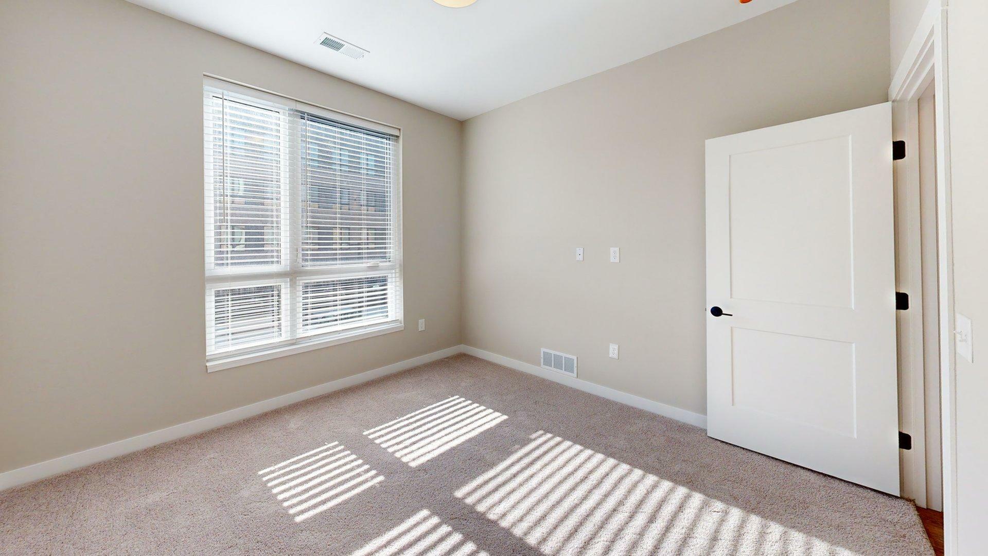 Bright and inviting room with large windows and soft carpet, perfect for a cozy bedroom or serene office space.