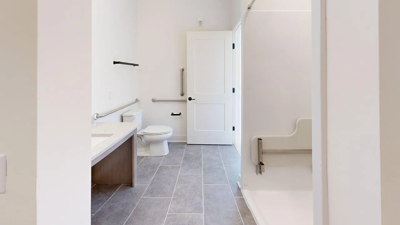 Elegant bathroom with modern fixtures, featuring a spacious shower, sleek tiled flooring, and convenient grab bars for accessibility.