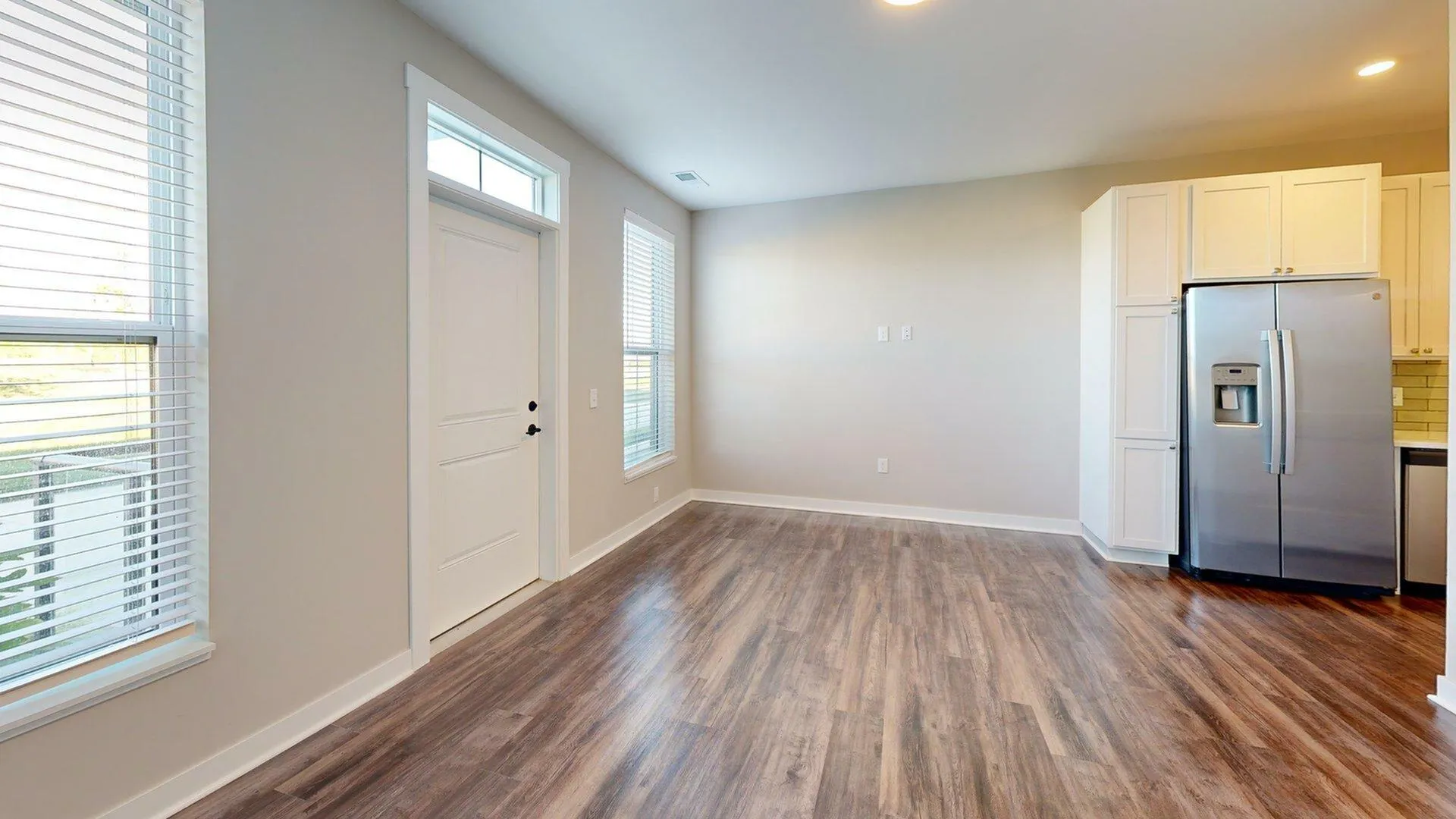 Bright and modern kitchen entrance with sleek stainless steel fridge, large windows, and elegant hardwood flooring.
