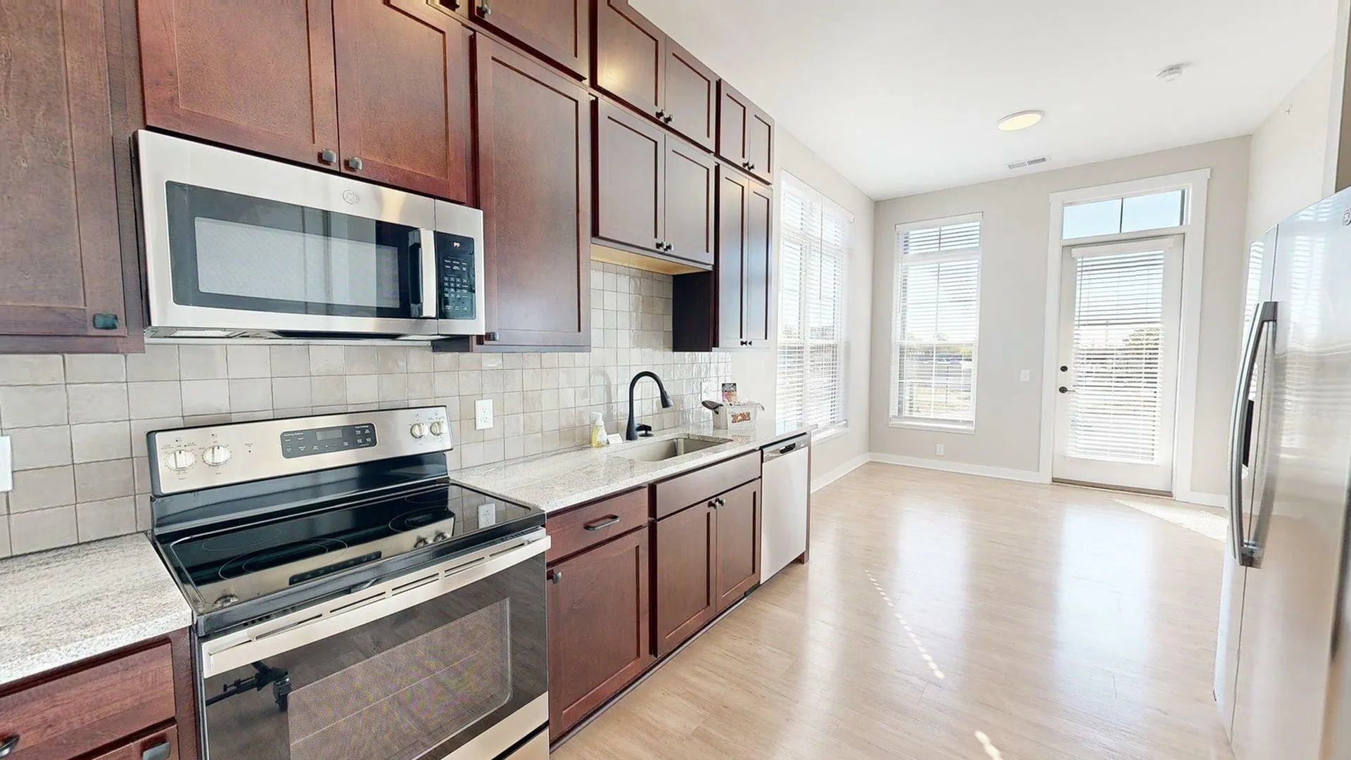 Bright, modern kitchen featuring elegant dark wood cabinets, sleek stainless steel appliances, and a spacious layout with abundant natural light.