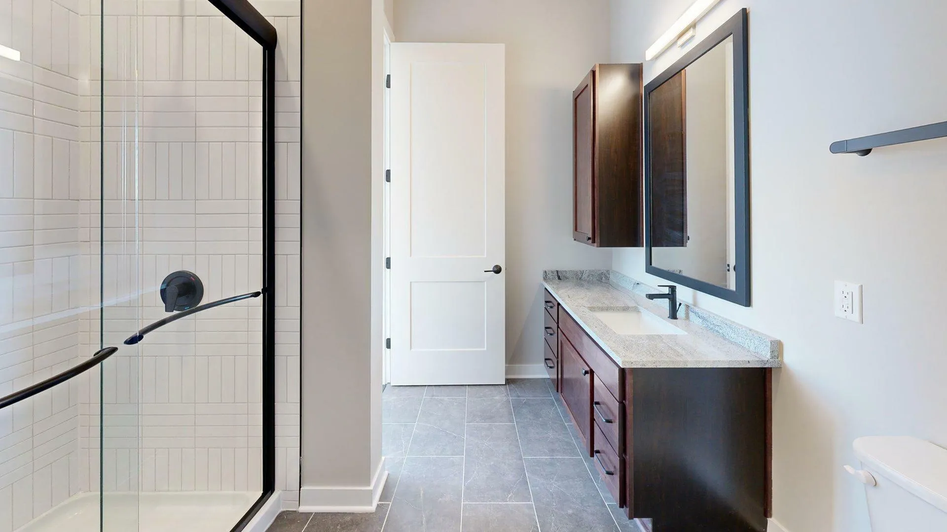 Elegant bathroom featuring a modern glass shower, dark wood vanity, large mirror, and sleek tile flooring.