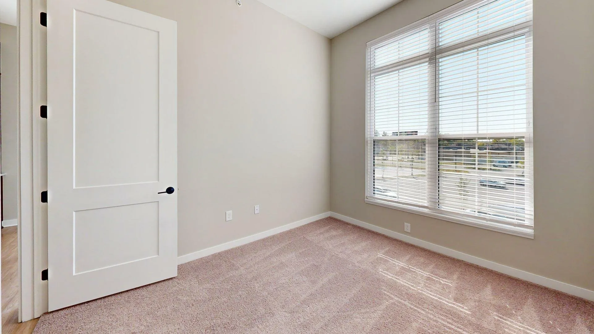 Bright and airy room with plush carpet and large window, perfect for a cozy home office or bedroom.