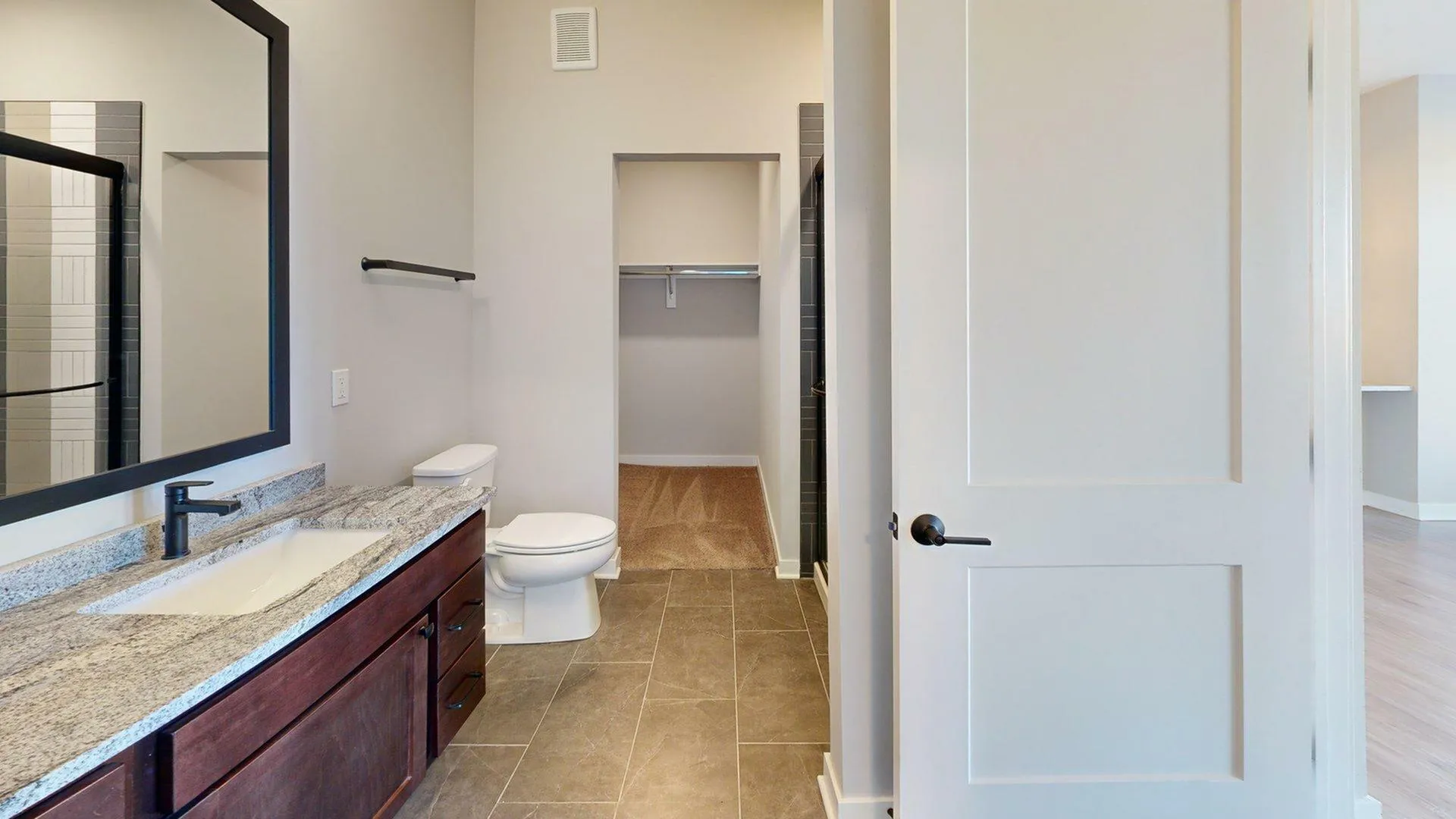 Modern bathroom with sleek gray tiles, granite countertop, and a spacious walk-in closet.