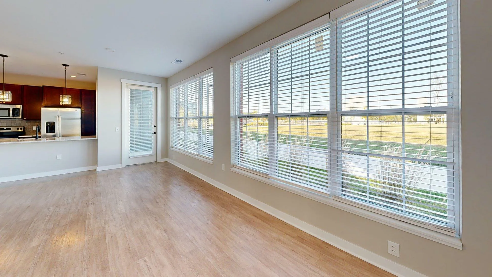 Bright apartment interior featuring large windows with blinds, modern kitchen with stainless steel appliances, and elegant light fixtures.