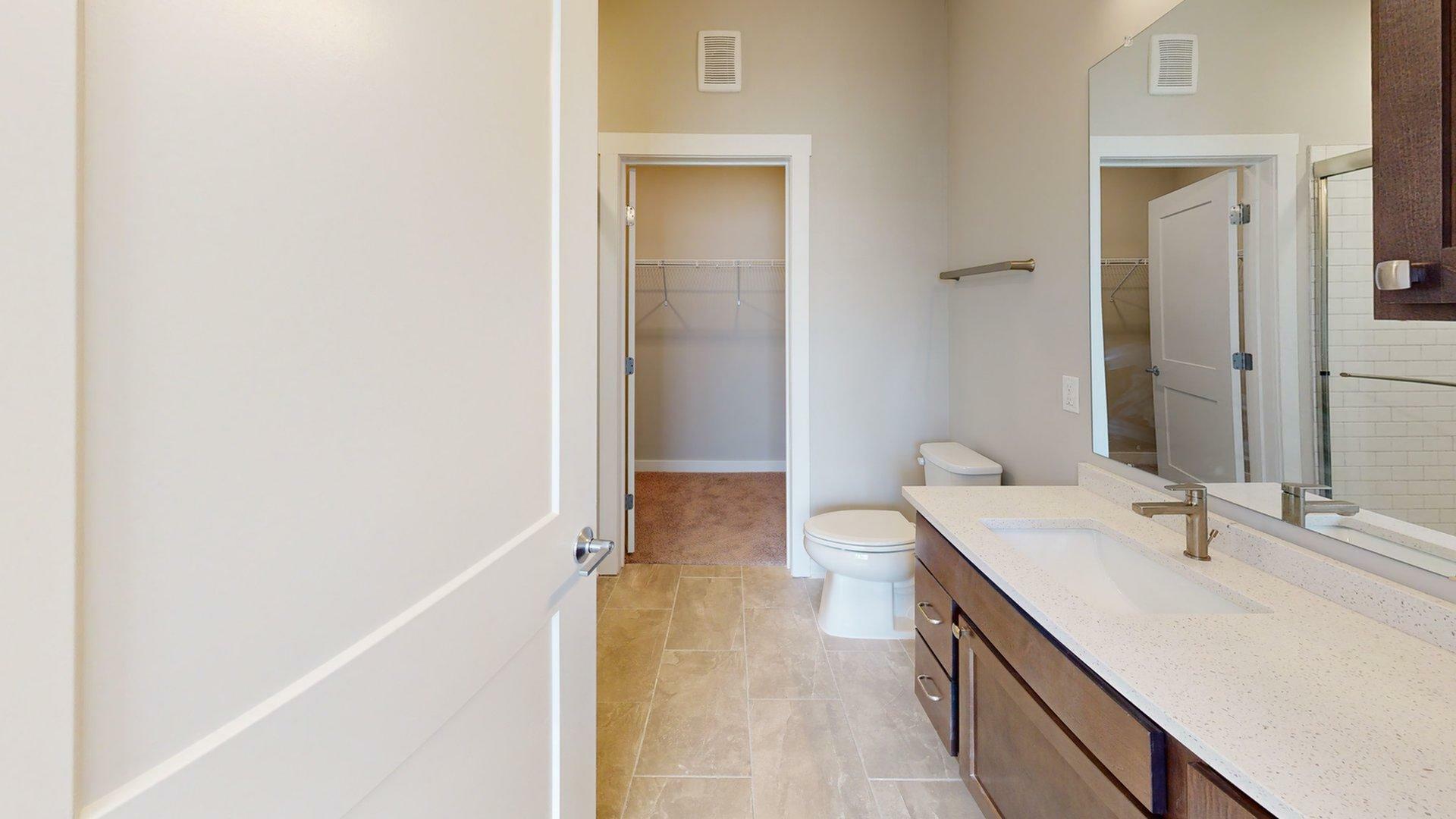 Modern bathroom featuring sleek vanity, spacious mirror, and convenient walk-in closet.