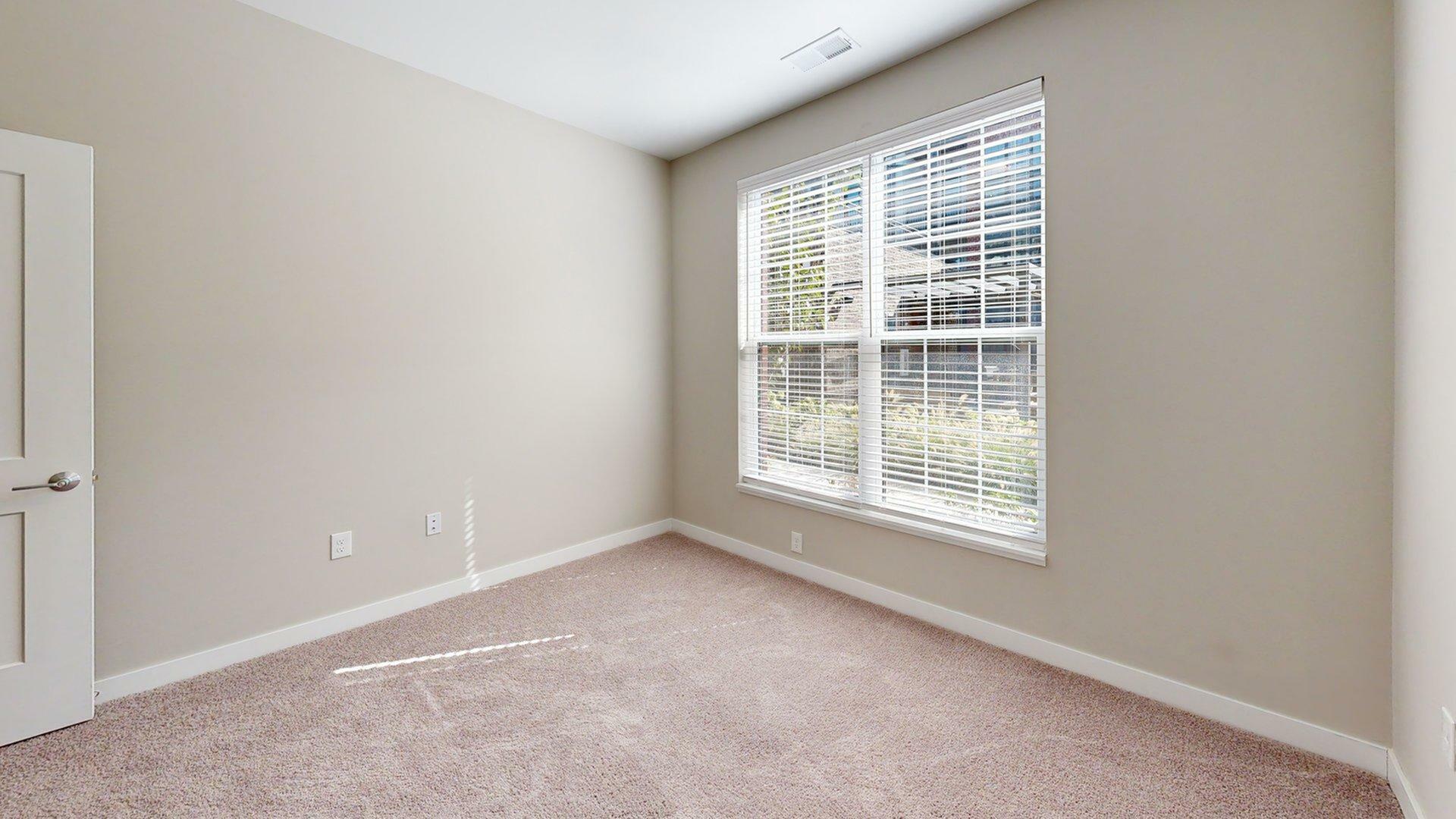 Sunlit room with neutral carpet and large window, perfect for creating a cozy bedroom or home office.