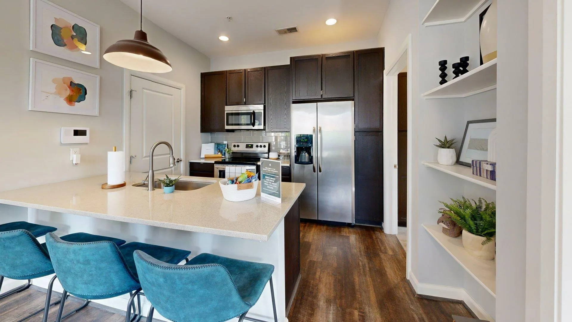 Modern kitchen with sleek dark cabinets and stainless steel appliances. Features a stylish breakfast bar with chic blue chairs and elegant decor, creating a warm and inviting atmosphere.