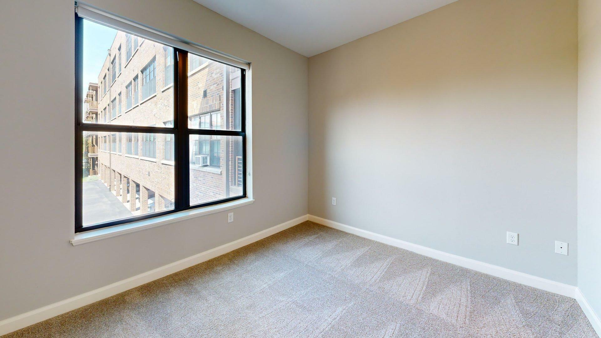 Bright and inviting room with large window offering urban views, perfect for a cozy bedroom or home office.