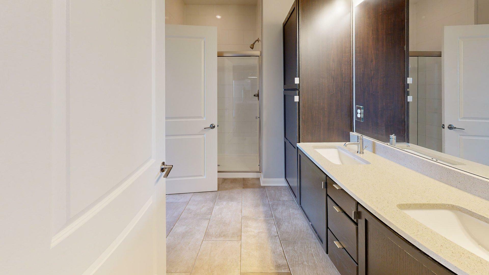Elegant apartment bathroom featuring a modern double sink vanity, spacious shower, and stylish dark wood cabinetry.