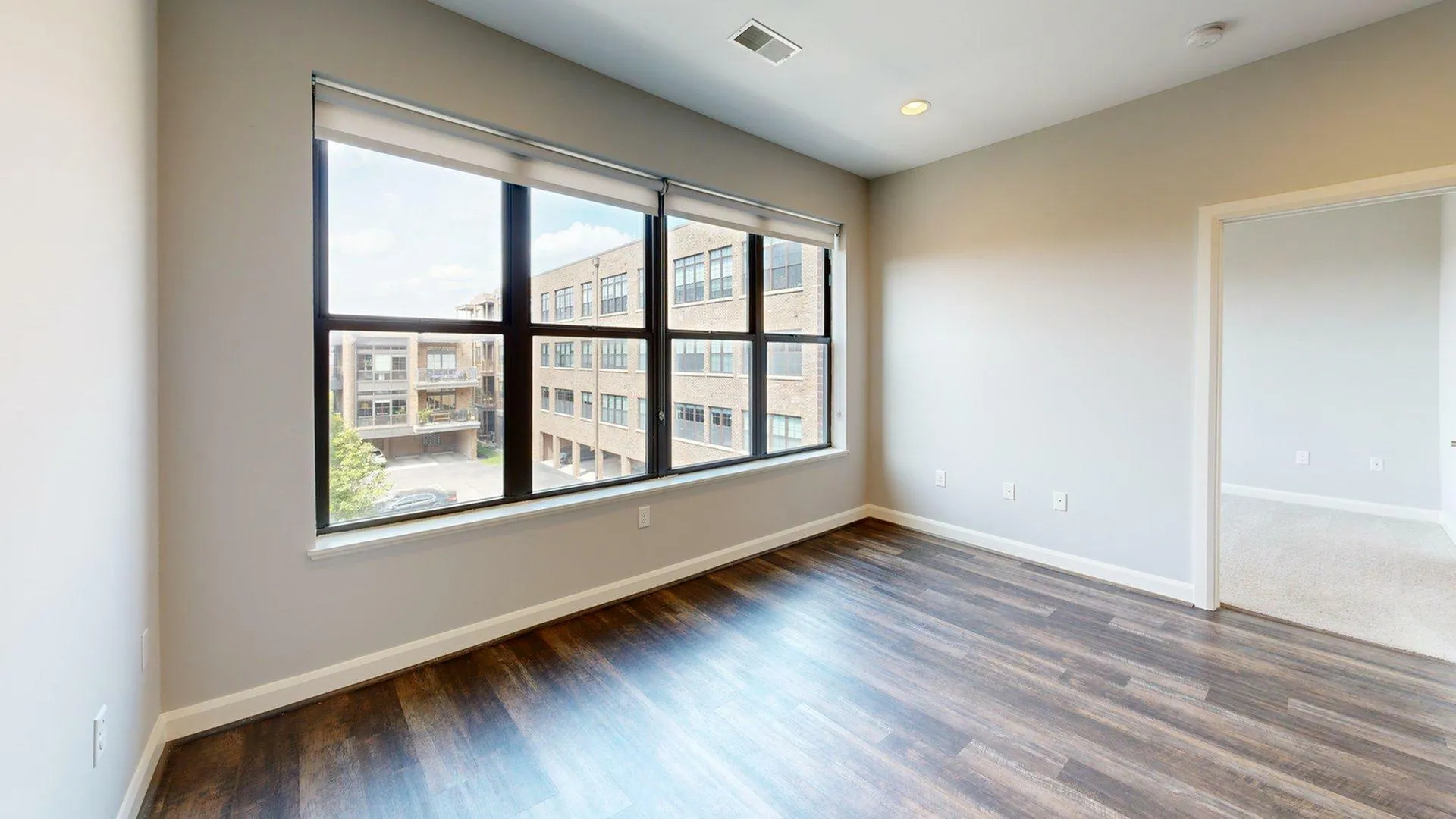 Bright and spacious room with large windows and modern wood flooring, offering plenty of natural light and a view of a stylish urban building.