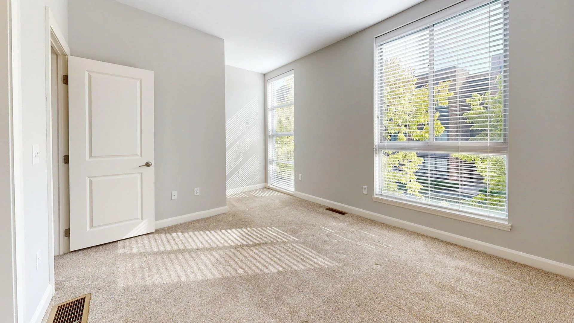 Bright and airy room with plush carpet, large windows with blinds, and neutral walls, perfect for a cozy and inviting atmosphere.