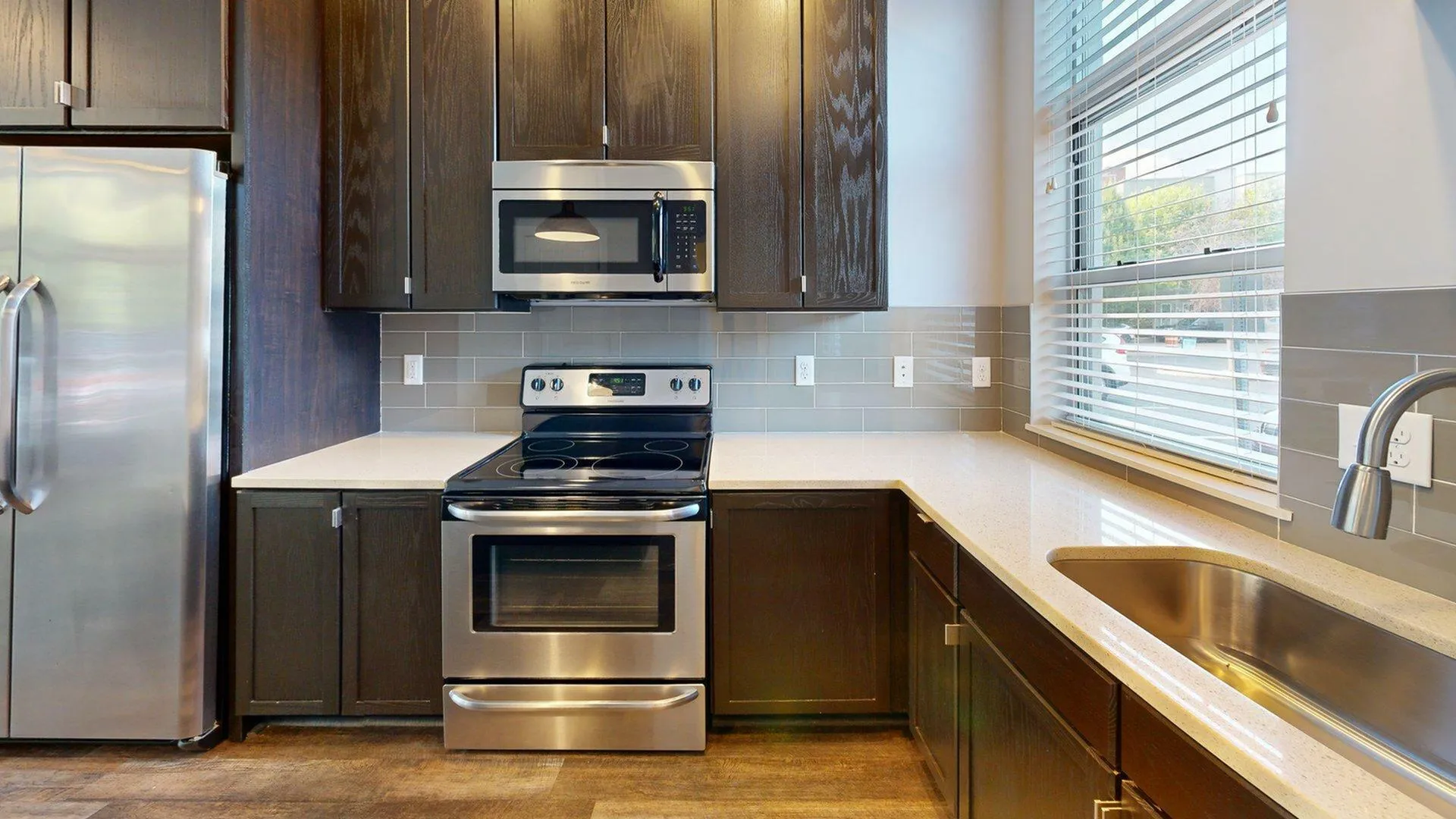 Modern kitchen with sleek stainless steel appliances, elegant dark wood cabinets, and ample natural light from large window.