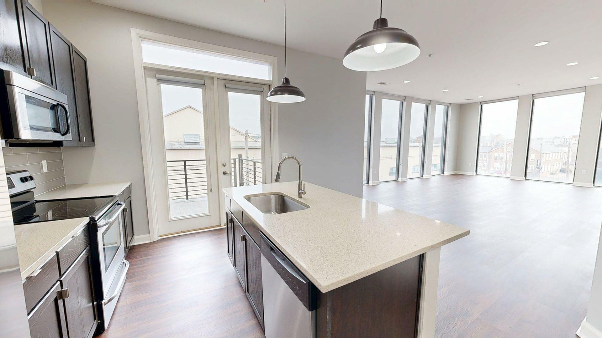 Modern open-concept kitchen and living space with sleek countertops, pendant lighting, and floor-to-ceiling windows offering abundant natural light.