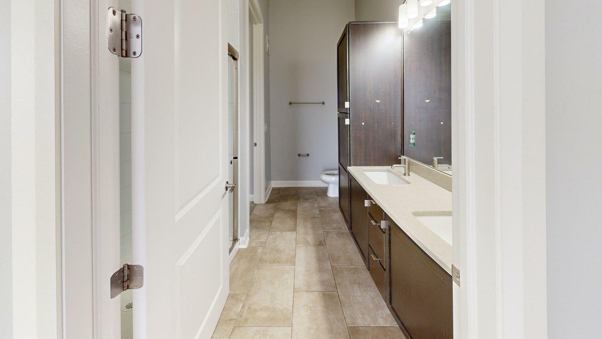 Modern bathroom featuring double sinks, sleek dark wood cabinetry, and elegant tile flooring, offering a stylish and functional space.