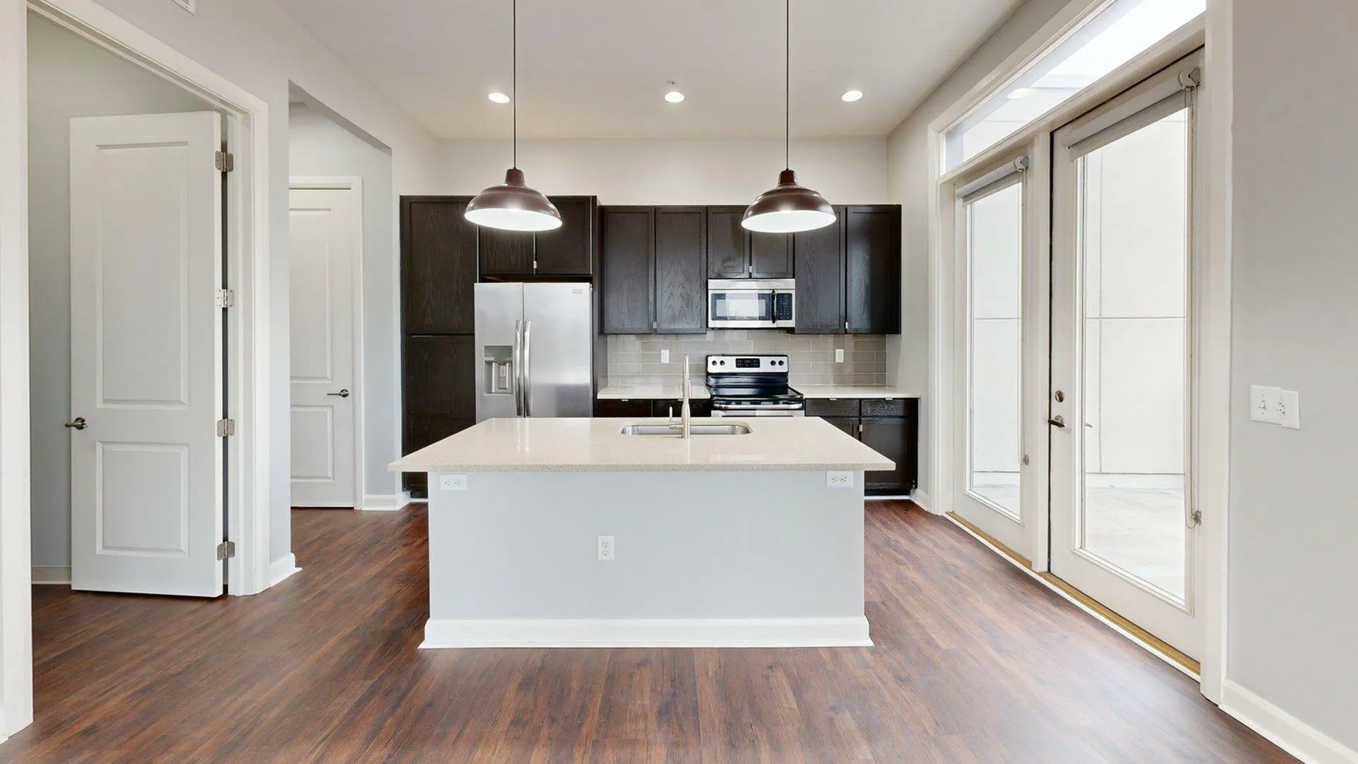 Modern kitchen with dark wood cabinets, stainless steel appliances, and a spacious island under stylish pendant lighting.