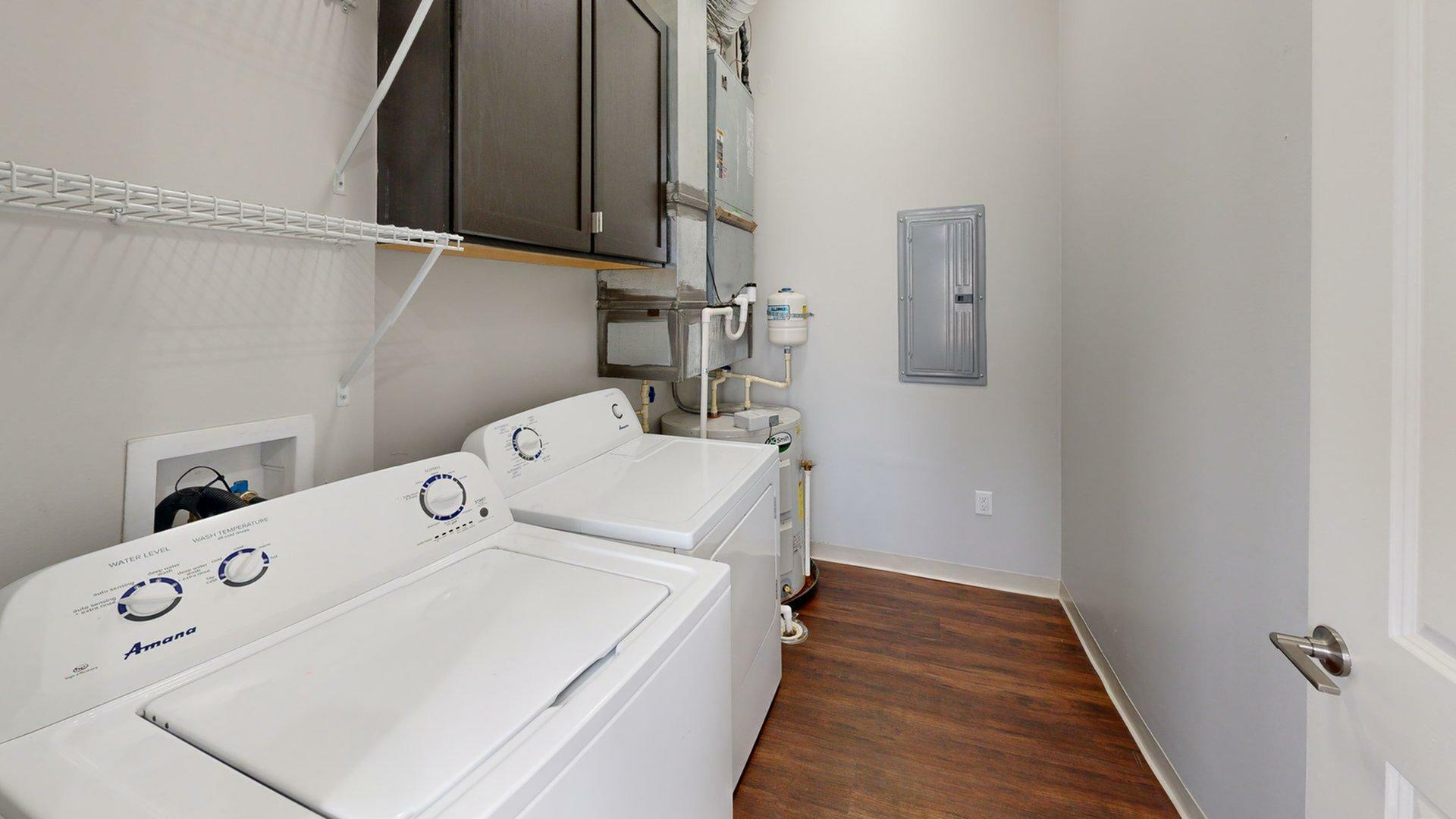 Modern laundry room with sleek hardwood flooring, equipped with washer and dryer, ample cabinetry, and efficient shelving.