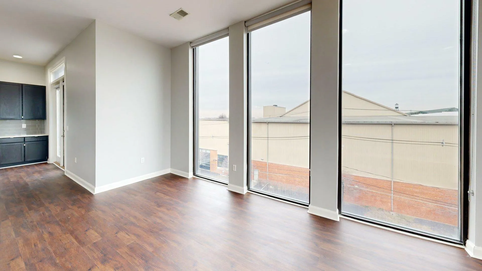 Bright and spacious living area with floor-to-ceiling windows, elegant wood flooring, and sleek dark cabinetry in the open kitchen.