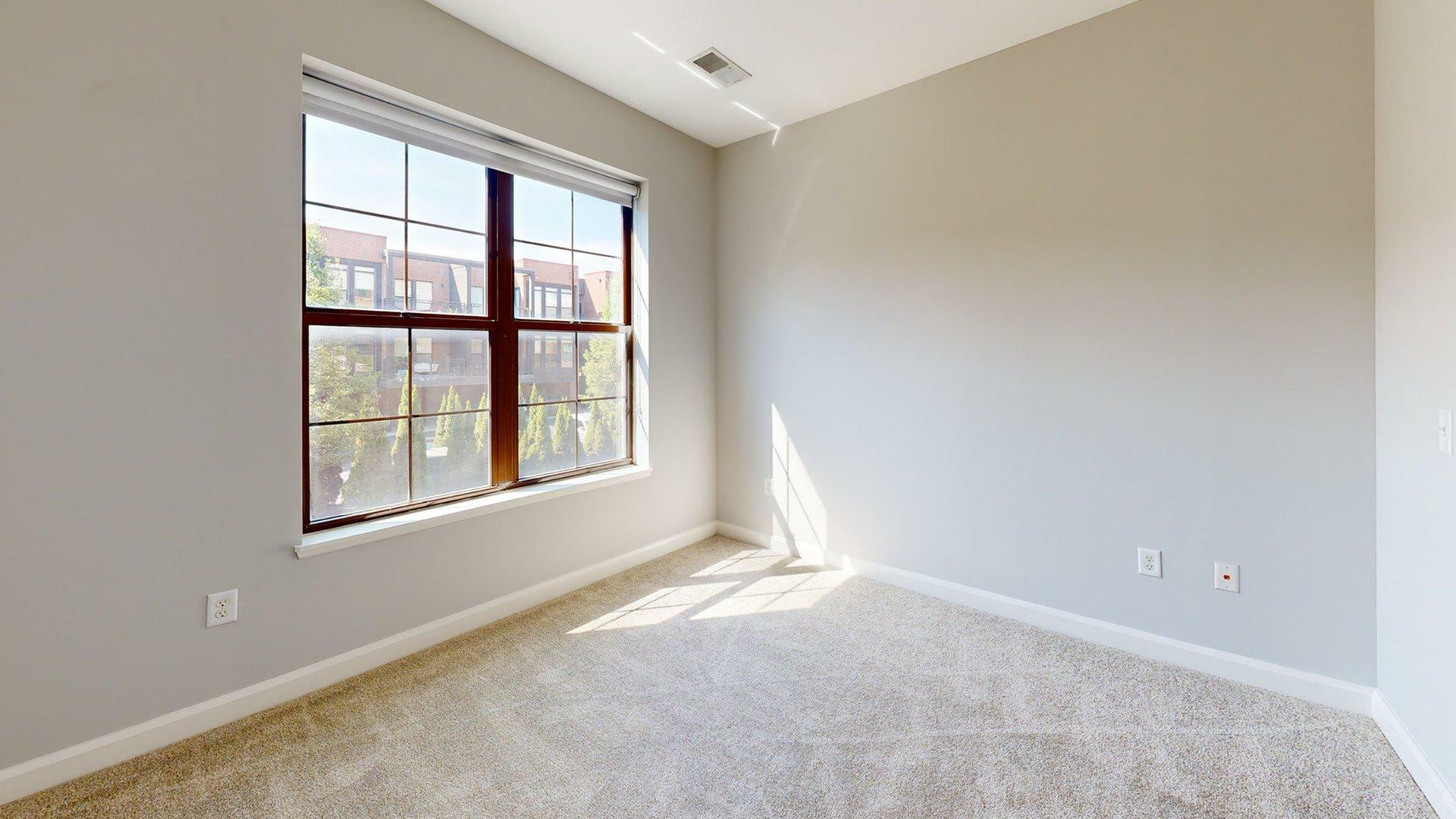 Bright and cozy room with a large window, carpeted floor, and soft natural light streaming in.