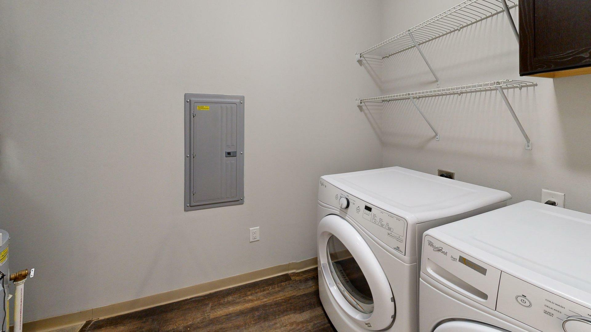 Modern laundry room featuring sleek washer and dryer, spacious shelving, and warm wooden flooring.