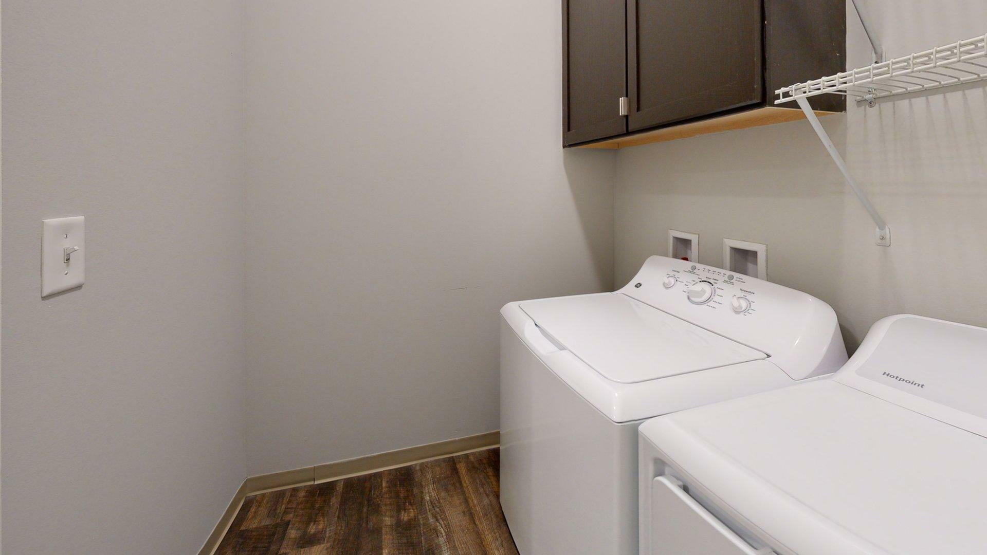 Modern laundry room featuring a sleek washer and dryer with ample cabinet and shelf space.