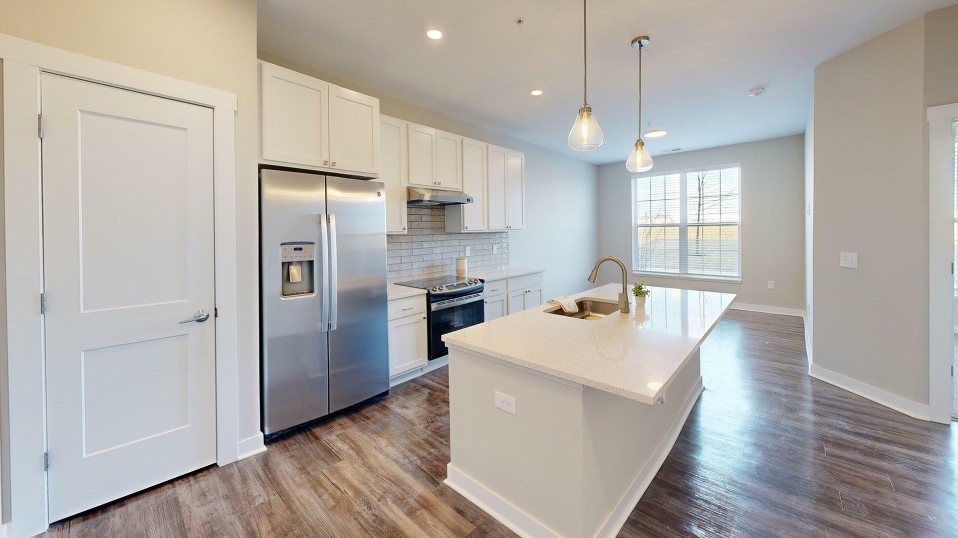 Modern kitchen with sleek stainless steel appliances, elegant cabinetry, and a spacious quartz island under stylish pendant lighting leading to a bright, open living space.