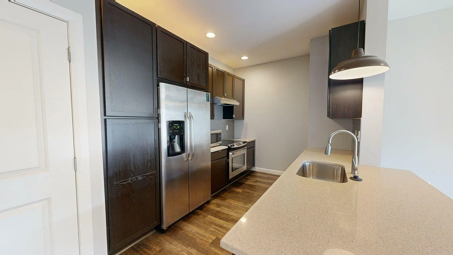 Modern kitchen featuring sleek dark cabinetry, stainless steel appliances, and a charming breakfast bar with pendant lighting.